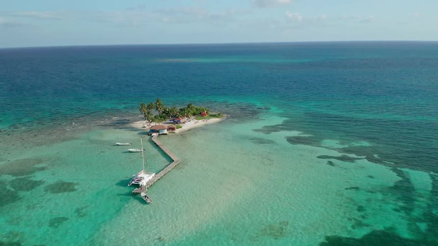A sandy island with long pier is surrounded by ocean water