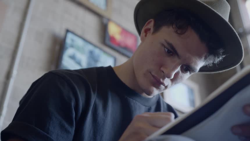 Man wearing a brimmed hat writes in a notebook