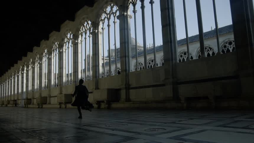 The silhouette of a man wearing a coat running past arches and columns