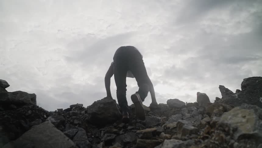 Black man hikes up on a steep rocky hill on a cloudy day