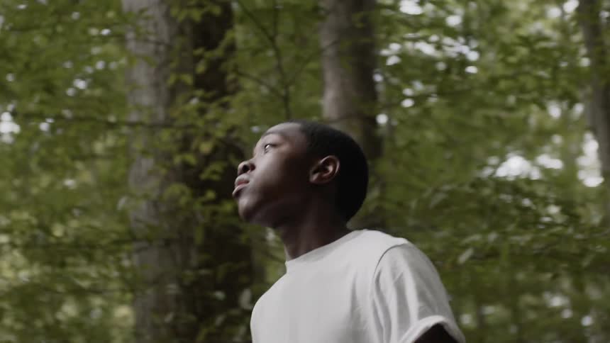 Black boy wearing a white t shirt walks on the forest track in the woods