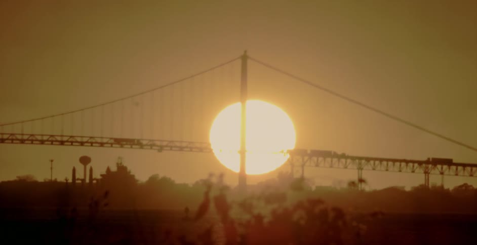 The sun sets behind a long bridge