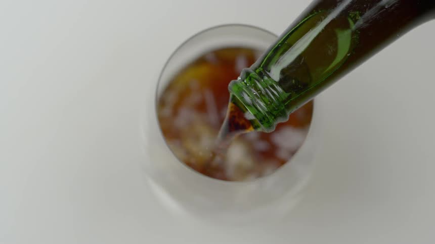 A beverage is being poured out of a bottle in to a glass