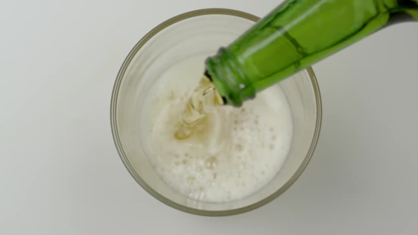Alochol foams up as it is poured into glass from green bottle