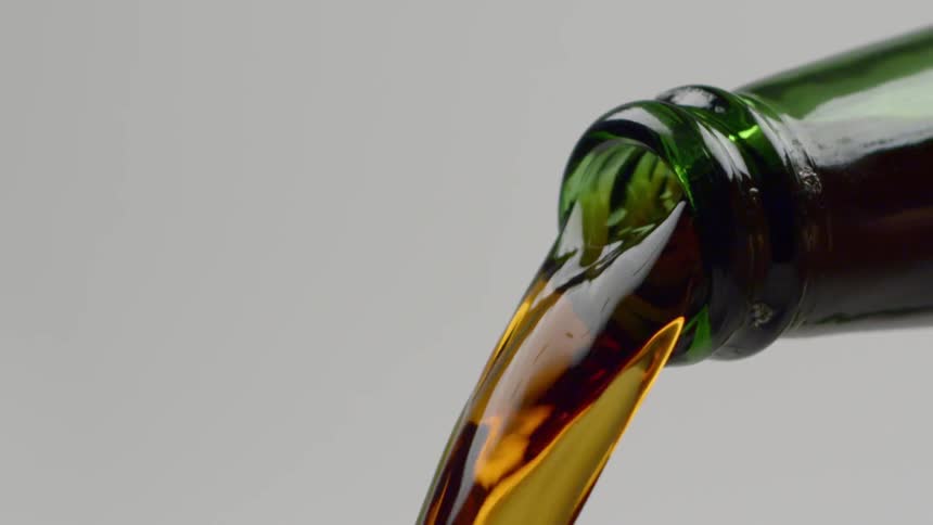 An amber beer is poured from a green glass bottle