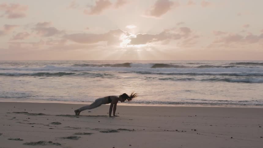 A woman does squat thrusts on the beach at sunset