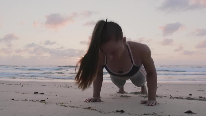 A woman does push ups on the beach at sunset