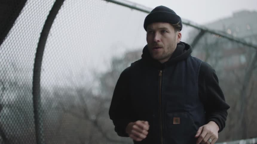 A man jogs across a fenced bridge in a city