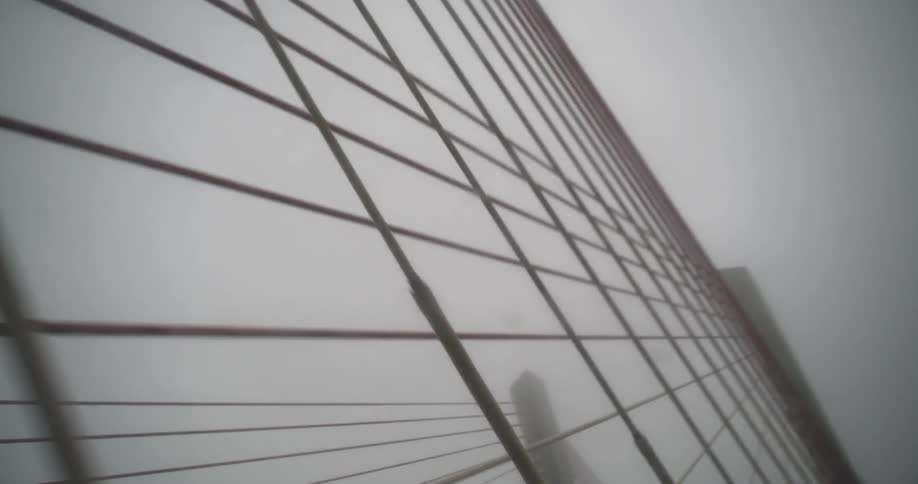 The suspension cables of a bridge seen through a cars windshield on a rainy day
