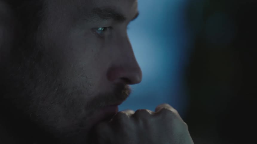 A man rubs his chin with his hand before typing on a laptop