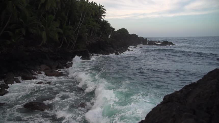 Waves crash against a rocky hillside on a cloudy day