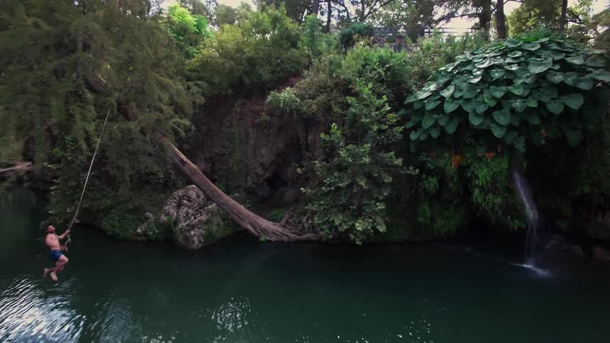 A young person swinging on a rope before jumping in a lake