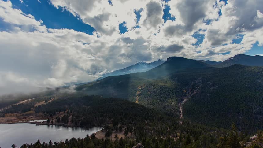 Clouds rolling over a forested mountain near a lake