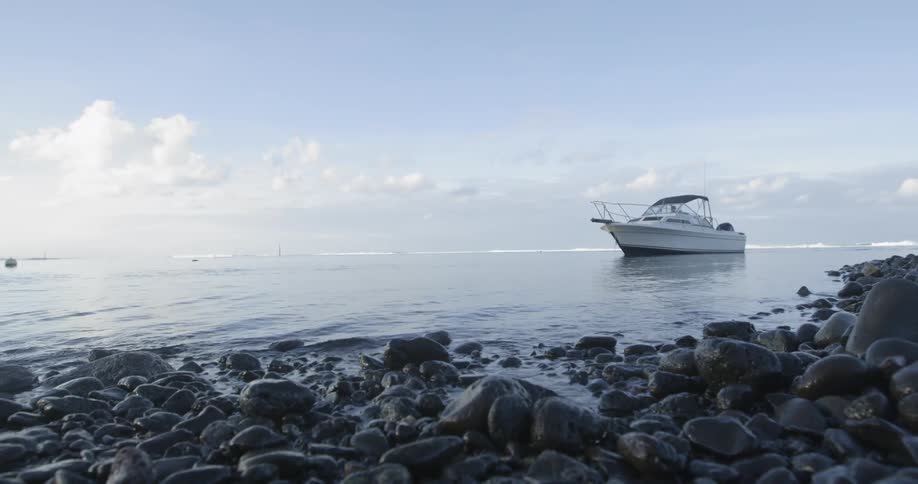 A recreational boat slowly glide along the ocean near a rocky shoreline