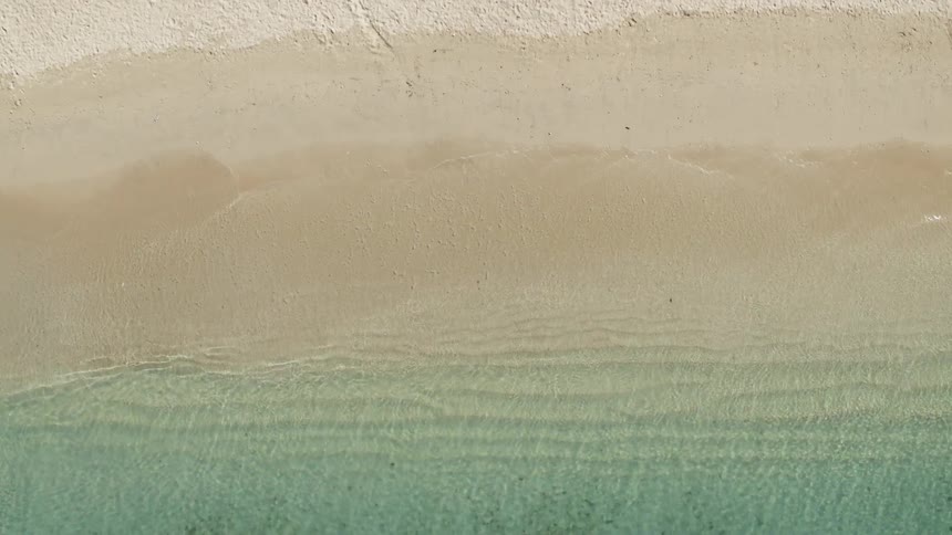 Birds eye view of gentle waves breaking softly on a sandy beach