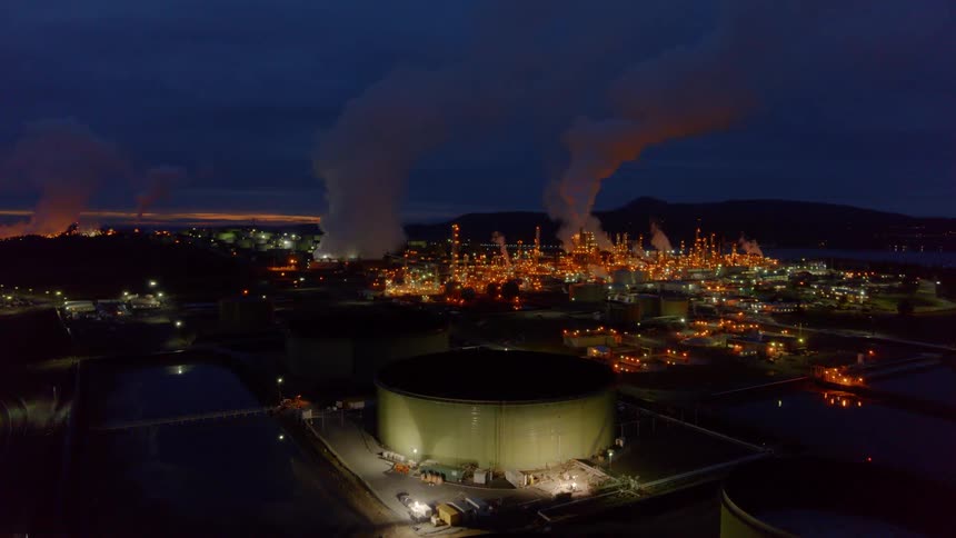 Flying over oil tanks toward a large petroleum refinery at dusk