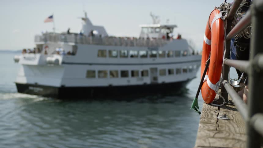 A multilevel boat carrying people moves past a pier with a life preserver attached to it