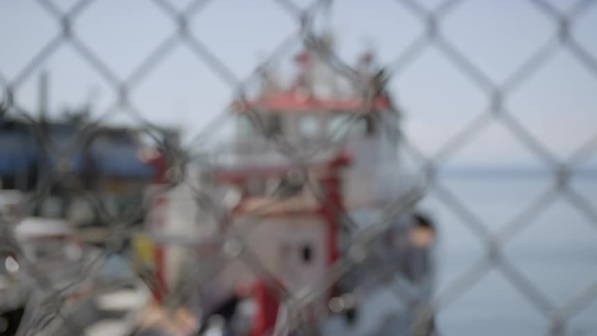 A large red and white ship is docked in an area behind a chain link fence