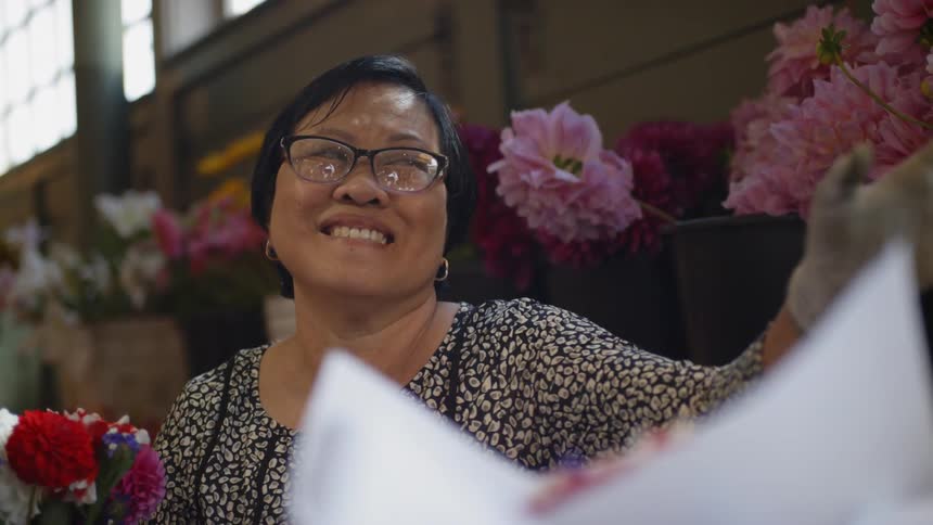 An asian woman paying for and bagging a bouquet of flowers