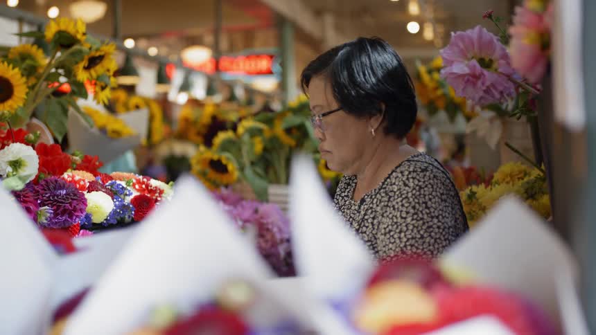 A woman stands at a flower stand at an indoor market