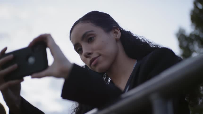 A woman smiles while holding a smartphone outside