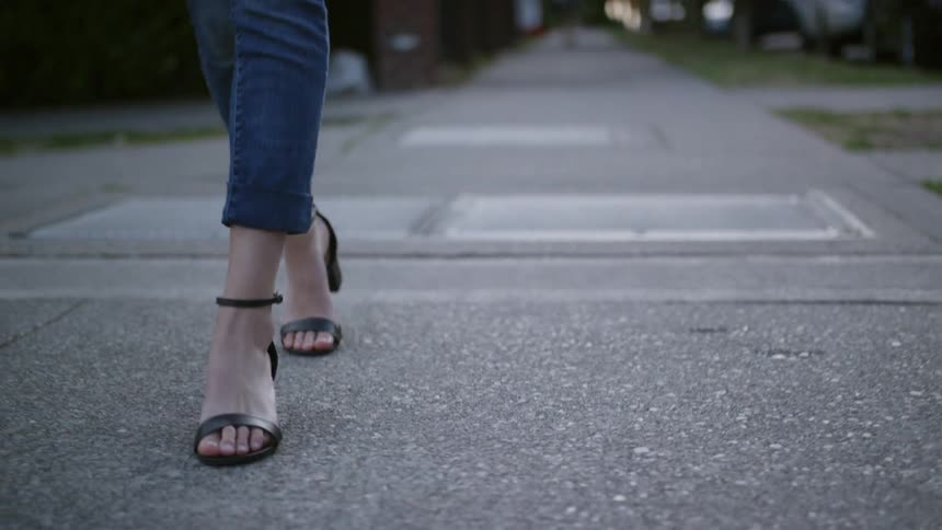 A woman wearing jeans and high heel black sandals walks down a sidewalk
