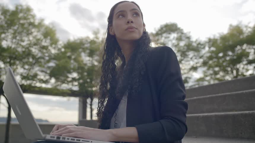 Brunette woman sitting on the stairs uses laptop on a cloudy day