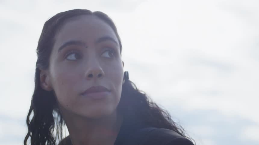Brunette woman wearing a wireless bluetooth earphone looks around on a cloudy day