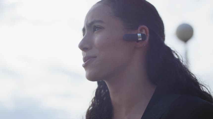 A woman wearing a blue tooth headset talks on her cell phone outside