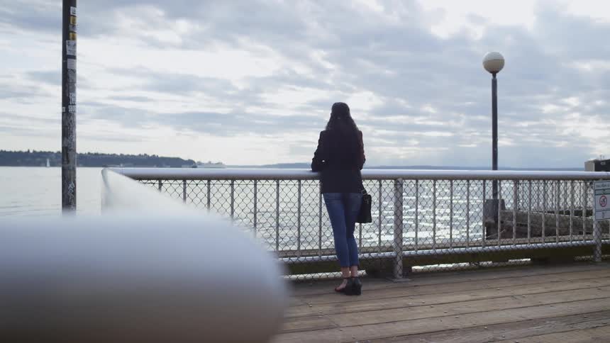 A woman standing on a pier looking at the ocean