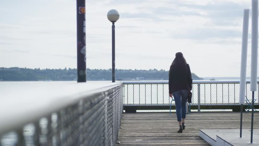 A woman walking on a boardwalk towards the handrail overlooking a body of water
