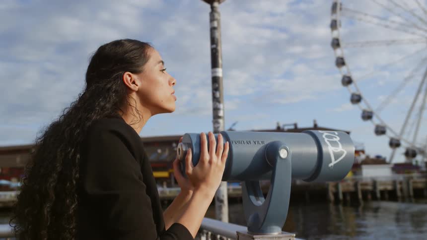 A woman is looking with a telescope outdoors at the landscape