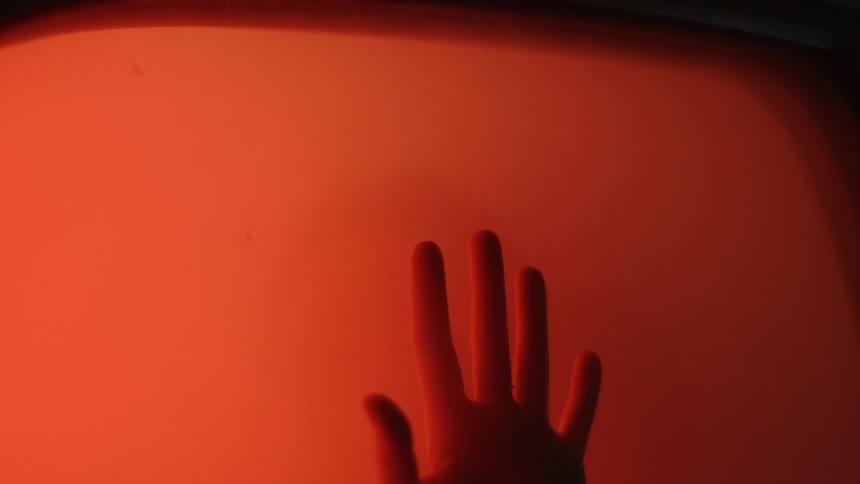 A hand is pressed against a red illuminated window