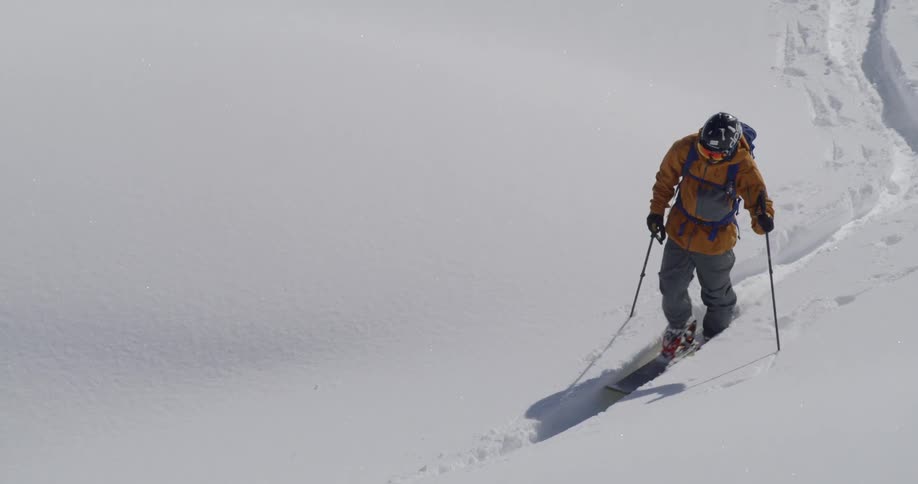 A man with yellow jacket walking with his snowboard