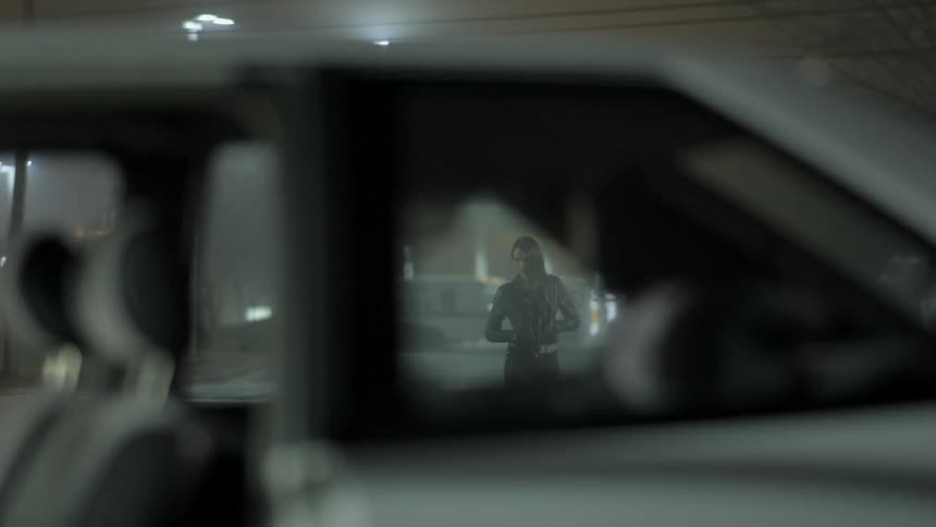 Shot looking through car windows to see a young woman pacing back and forth with an ambulance in the background