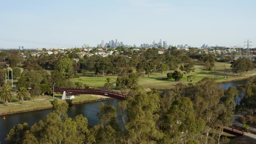 A walking bridge over a river outside of a large city
