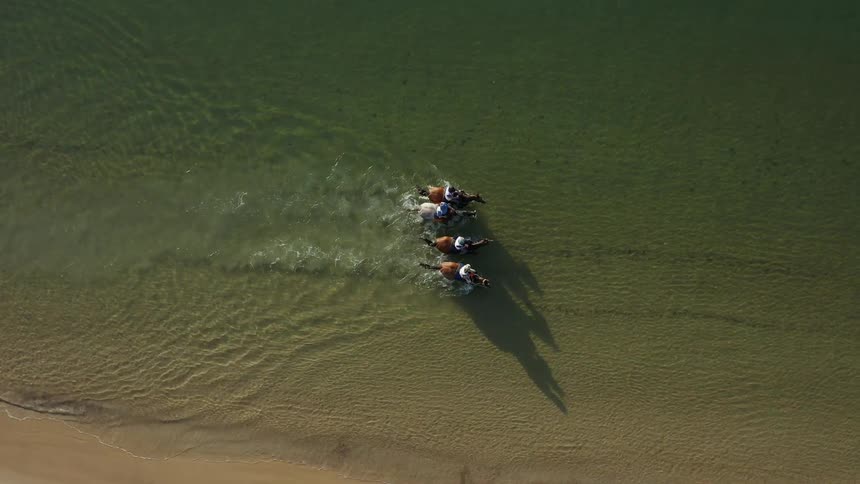 People ride horses in the water of the beach