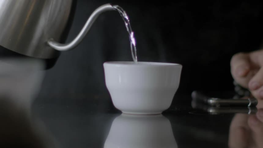 Water pouring into a small bowl from a tea kettle with long spout