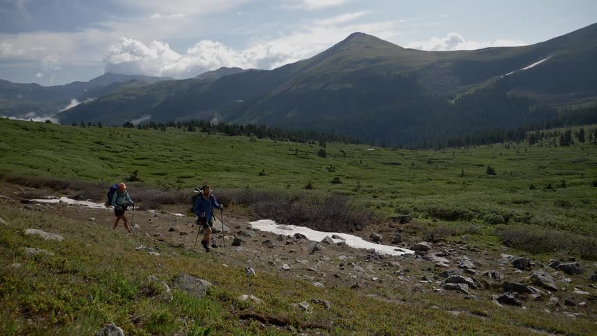 A pair of hikers crossing a plain below a mountain ridge