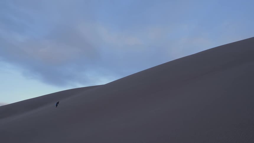 A person walking across sand dunes at low sun