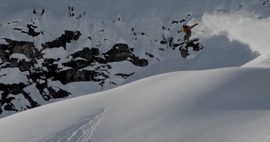 A skier jumps off a snow drift while skiing down a mountain