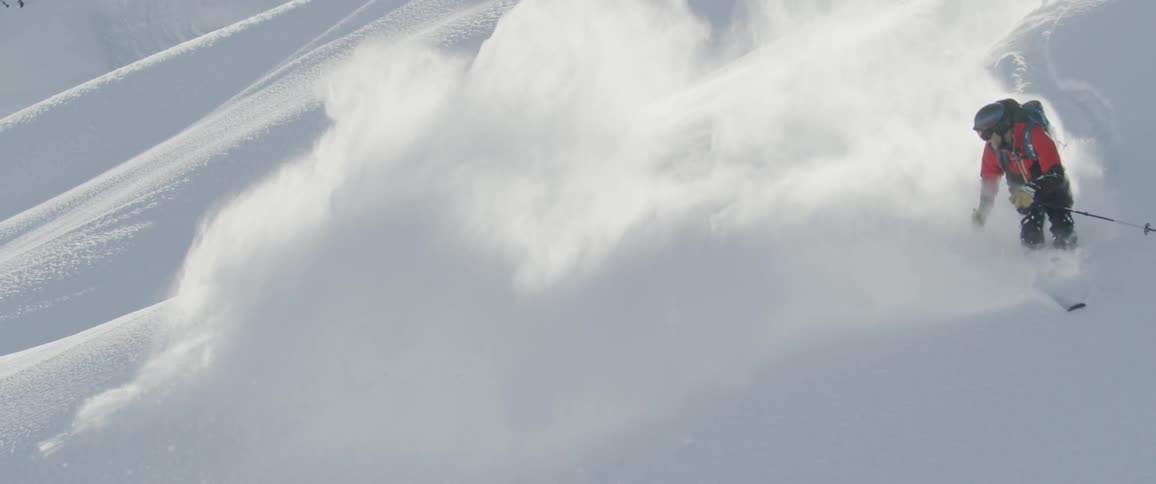 Skier kicks up snow as he skis down slope
