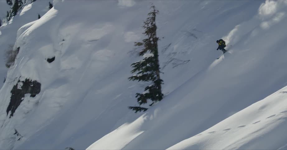 A person skis down a steep mountain lined with trees and boulders