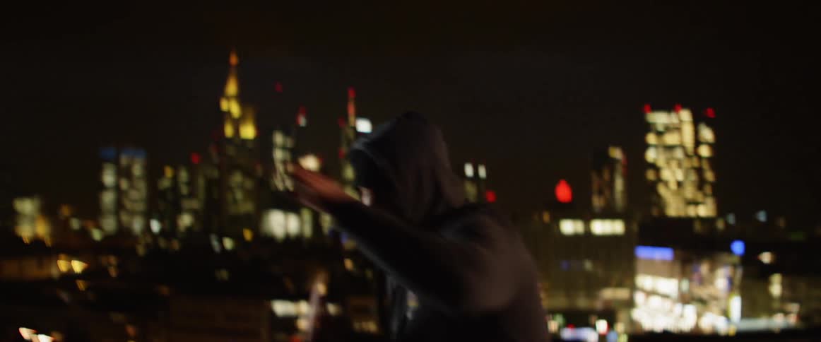 Man in a hoodie shadow boxing on the roof top at night in the city