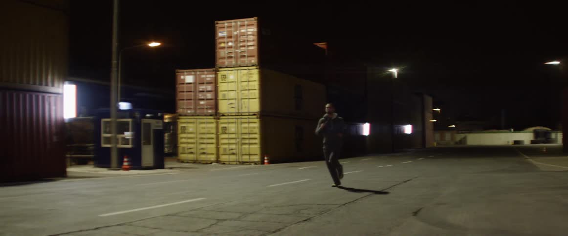 A man is running at night past a stack of cargo containers
