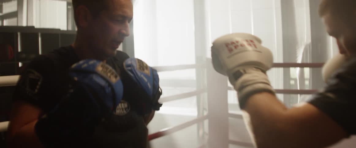 A boxer in a boxing ring punching a coaching vest held by a boxing coach