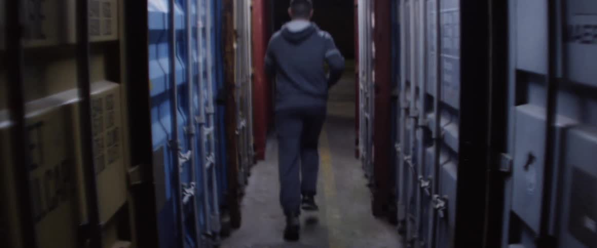 A man runs down a narrow hallway and through a doorway to go outside