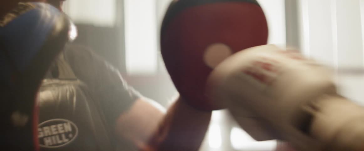 A man uses padded punch mitts to help train a boxer at the gym