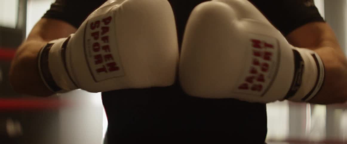Male wearing white boxing gloves brings his hands up and pounds the gloves together