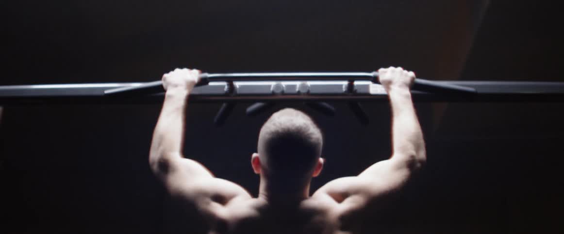 A man grabs onto a horizontal bar and does pull ups
